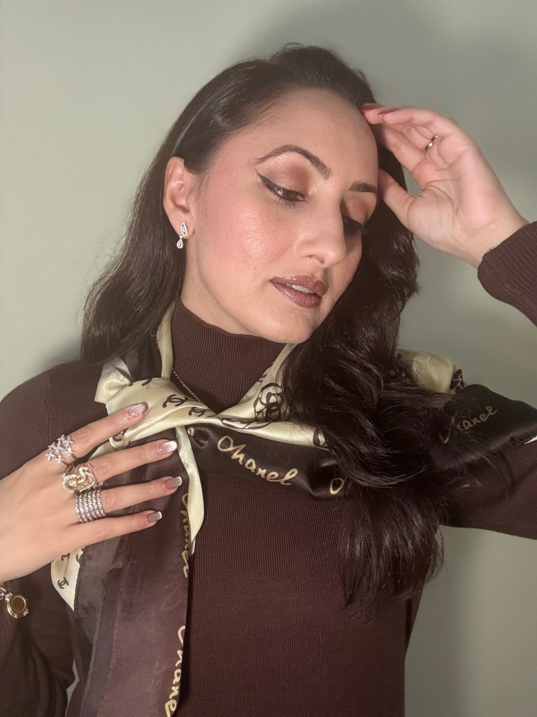 A woman wearing a fitted wool turtleneck tunic and silk Chanel scarf with signature motifs, showcasing her elegant style and accessories.